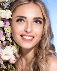 Beautiful blonde young woman with clean healthy skin on a face. Girl facial treatment. Bouquet of roses and other flowers