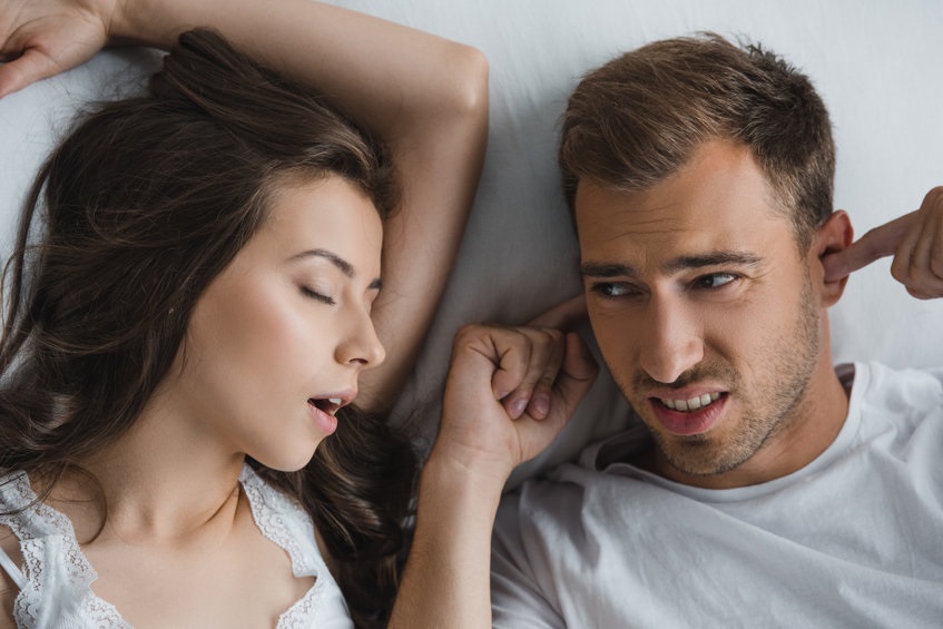 top view of man closing ears and looking at snoring wife in bed